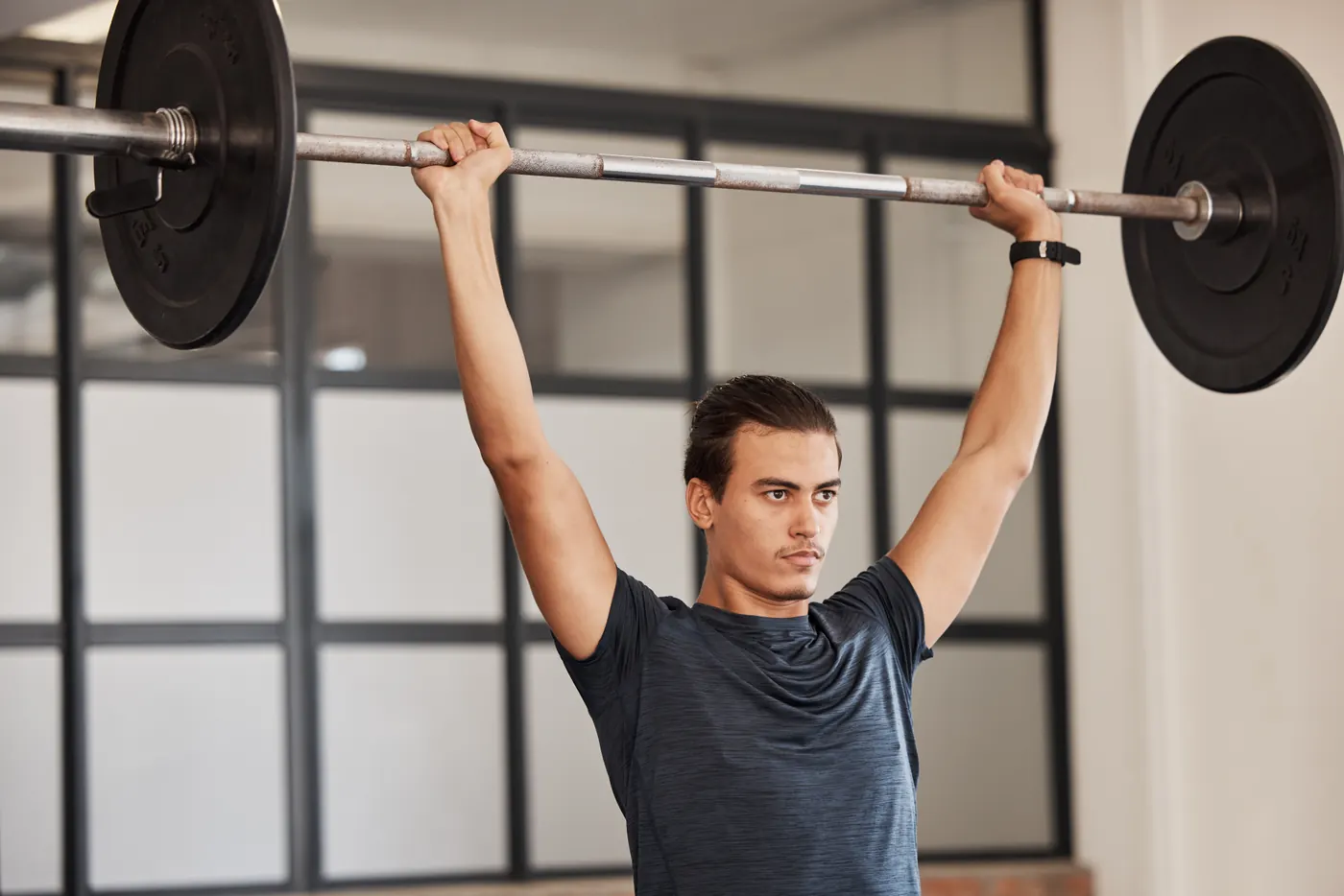 Strong man, overhead barbell and gym exercise, workout and fitness training in sports club. Young man, focus bodybuilder and power press, weightlifting challenge and muscle, motivation and energy