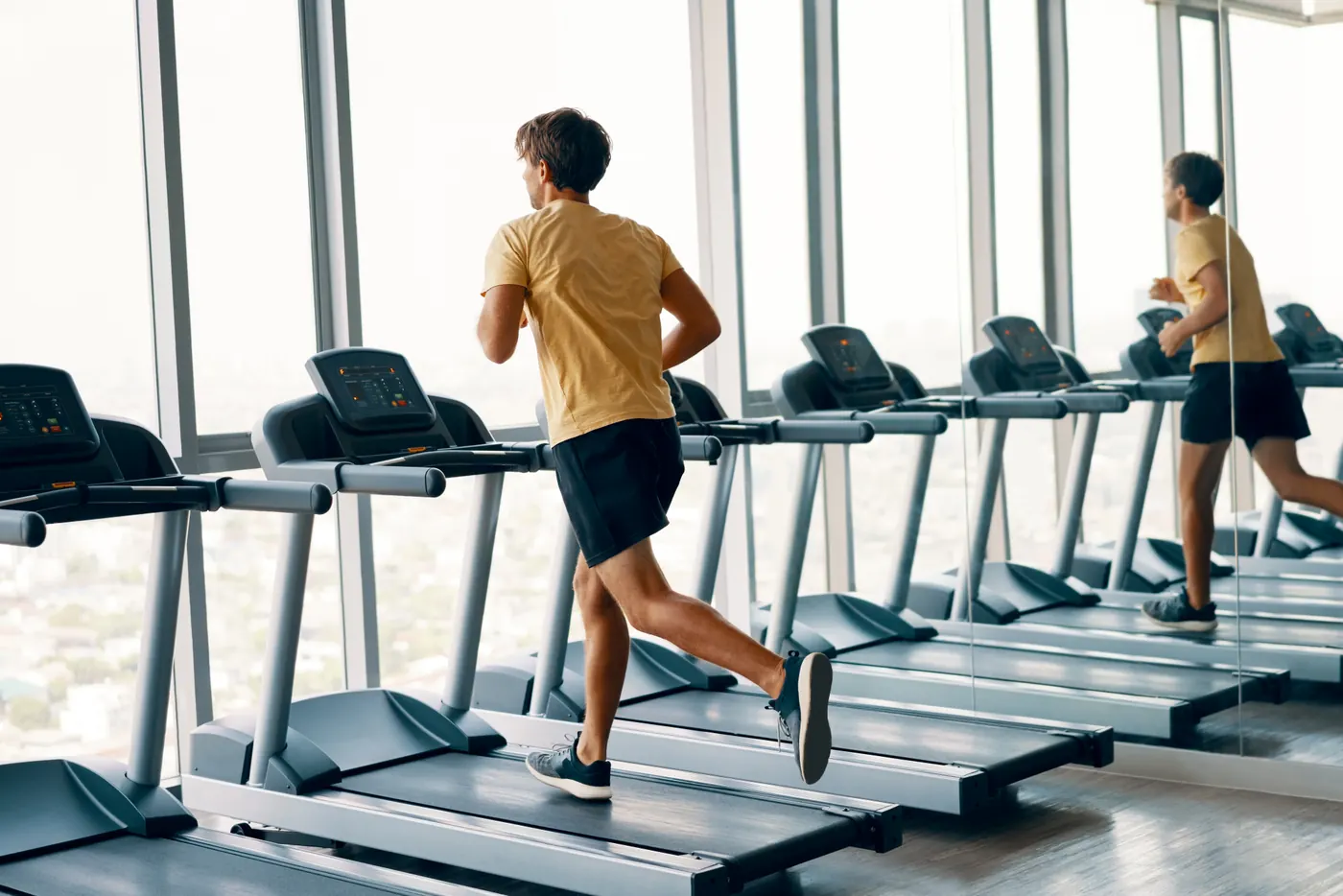 Full length portrait of young sports man running on a treadmill at gym