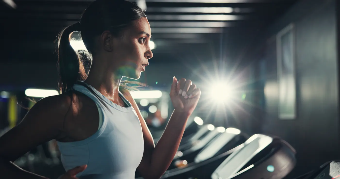 Workout, girl and running on treadmill in gym at night for fitness, training and burning calories. Flare, late exercise and athlete with breathing for intense cardio, endurance challenge and wellness