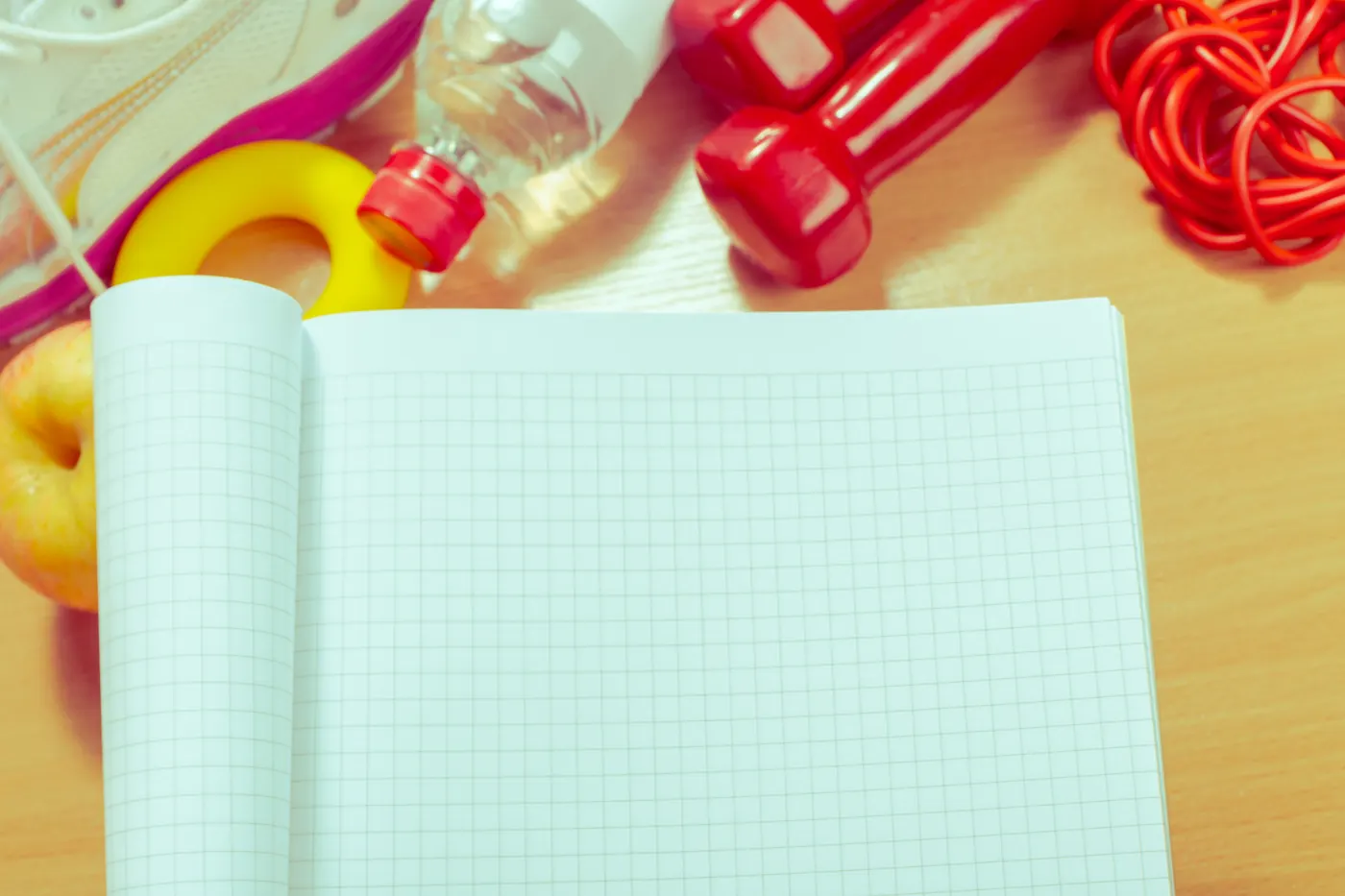 An open notebook beside dumbbells, a skipping rope and a water bottle